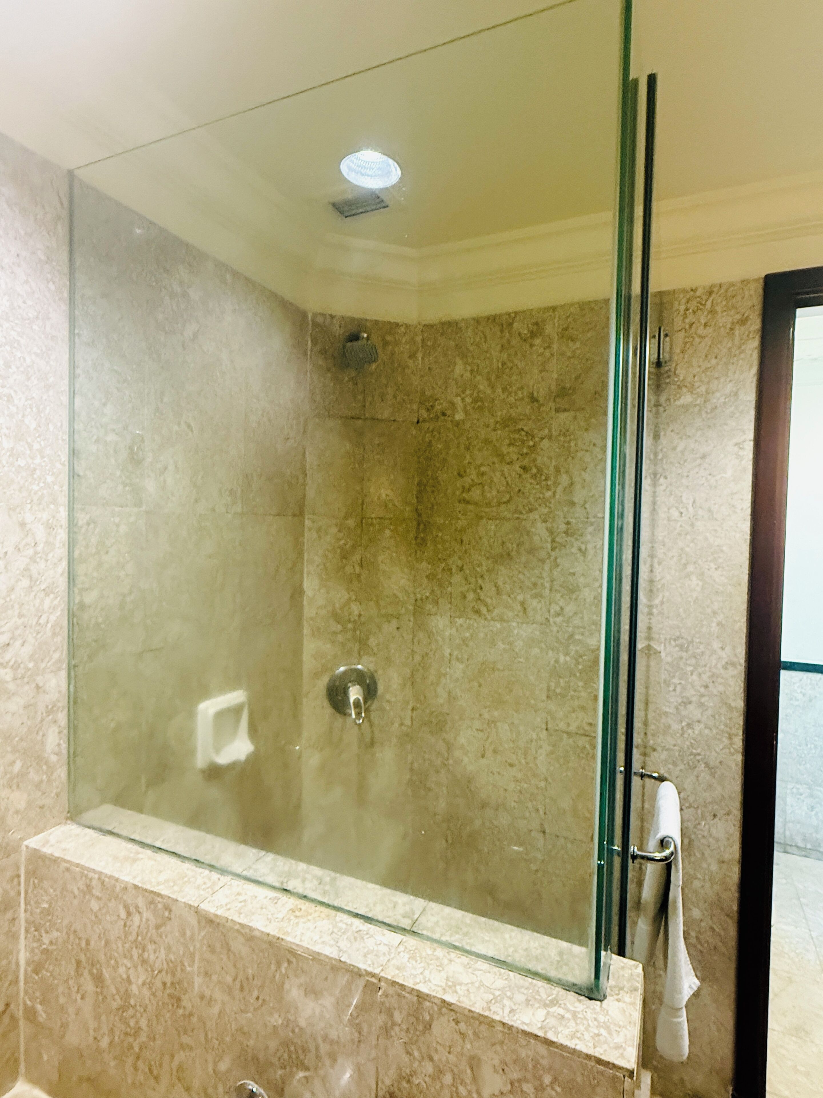 A glass-enclosed shower with a marble wall, a glass shelf, and a towel rack.