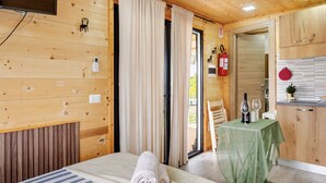 Una habitación de madera con una cama, una mesa con mantel verde y un rincón de cocina.