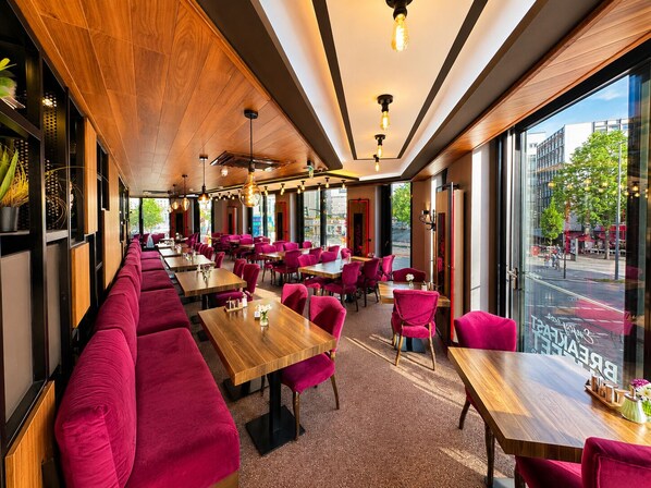 A modern restaurant interior with wooden ceiling, red upholstered seating, and large windows offering city views. - Nivara Hotel (Hamburg)