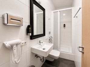 Un baño moderno con lavamanos, espejo y retrete blancos, un secador de manos y una zona de ducha.
