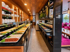 A buffet area with various food options, a coffee station, and seating area with tables and chairs. - Nivara Hotel (Hamburg)