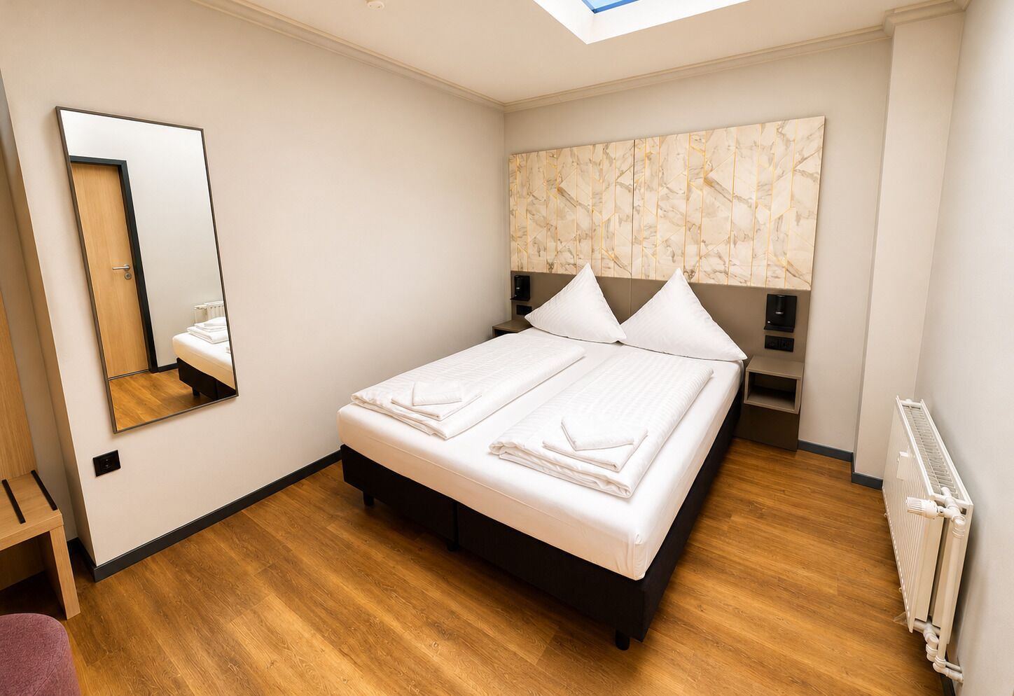 Una habitación de hotel moderna con una cama grande, un tragaluz, un cabecero con diseño de mármol y suelo de madera.