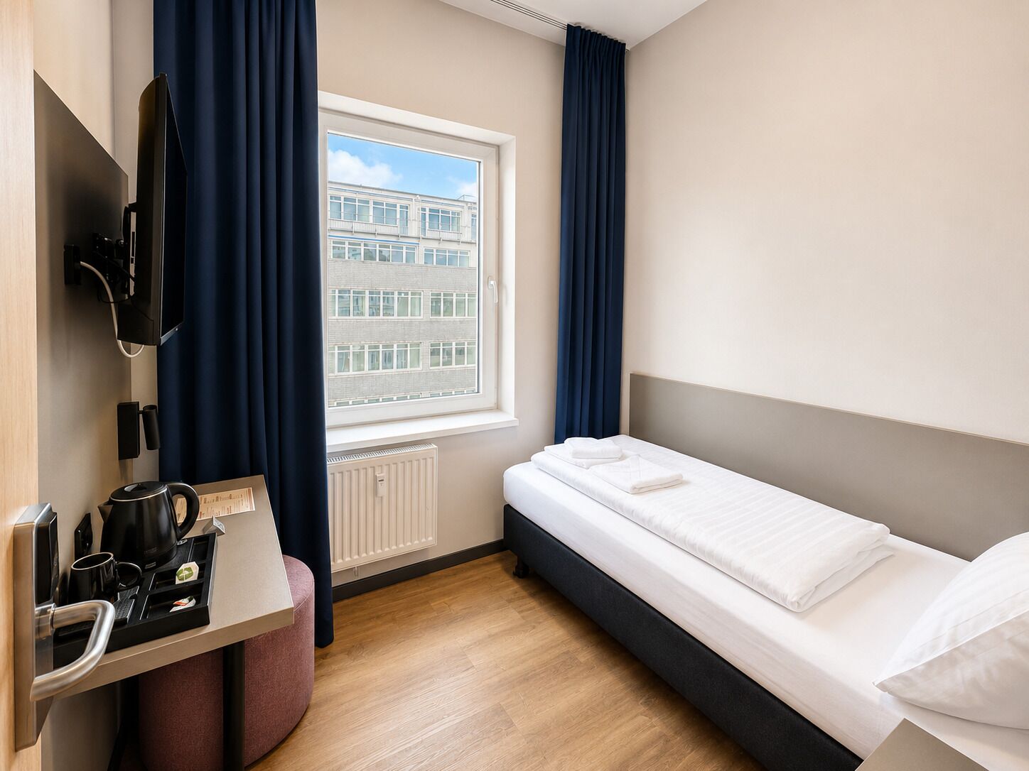 Una habitación de hotel con una cama, un escritorio con tetera, cafetera y una ventana con cortinas.