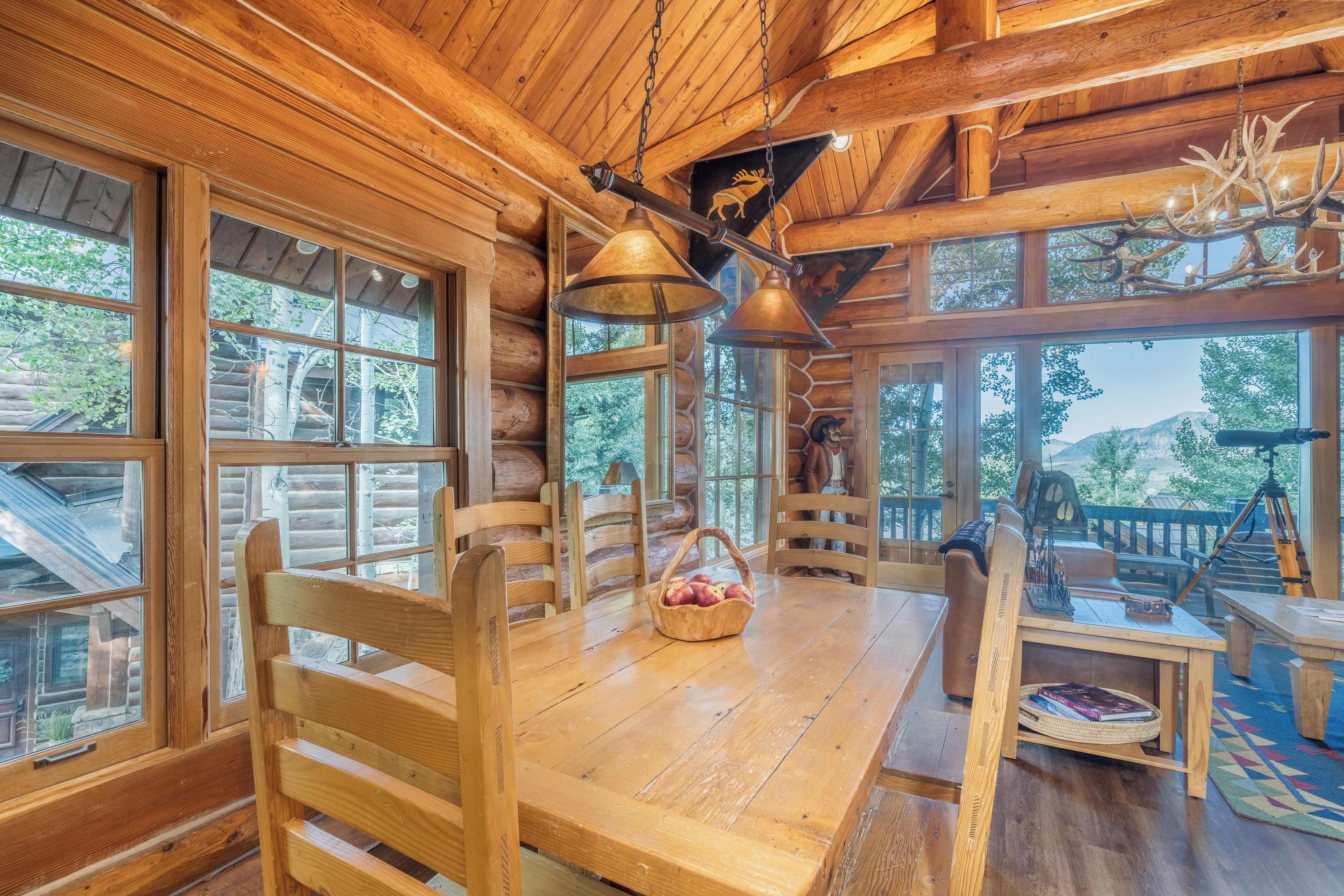 Ein Blockhaus-Interieur mit einem Holzesstisch, Stühlen und einer Pendelleuchte.