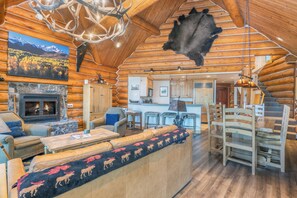 A log cabin interior with a stone fireplace, a sofa with a moose-patterned throw, a dining area, and a kitchen. - Summit Cabin - Luxury 3 BDR Condo w/ Sweeping Views (Telluride)