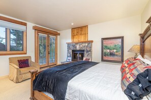 A bedroom with a large bed, a stone fireplace, wooden cabinets, and a window with a view of trees. - Summit Cabin - Luxury 3 BDR Condo w/ Sweeping Views (Telluride)