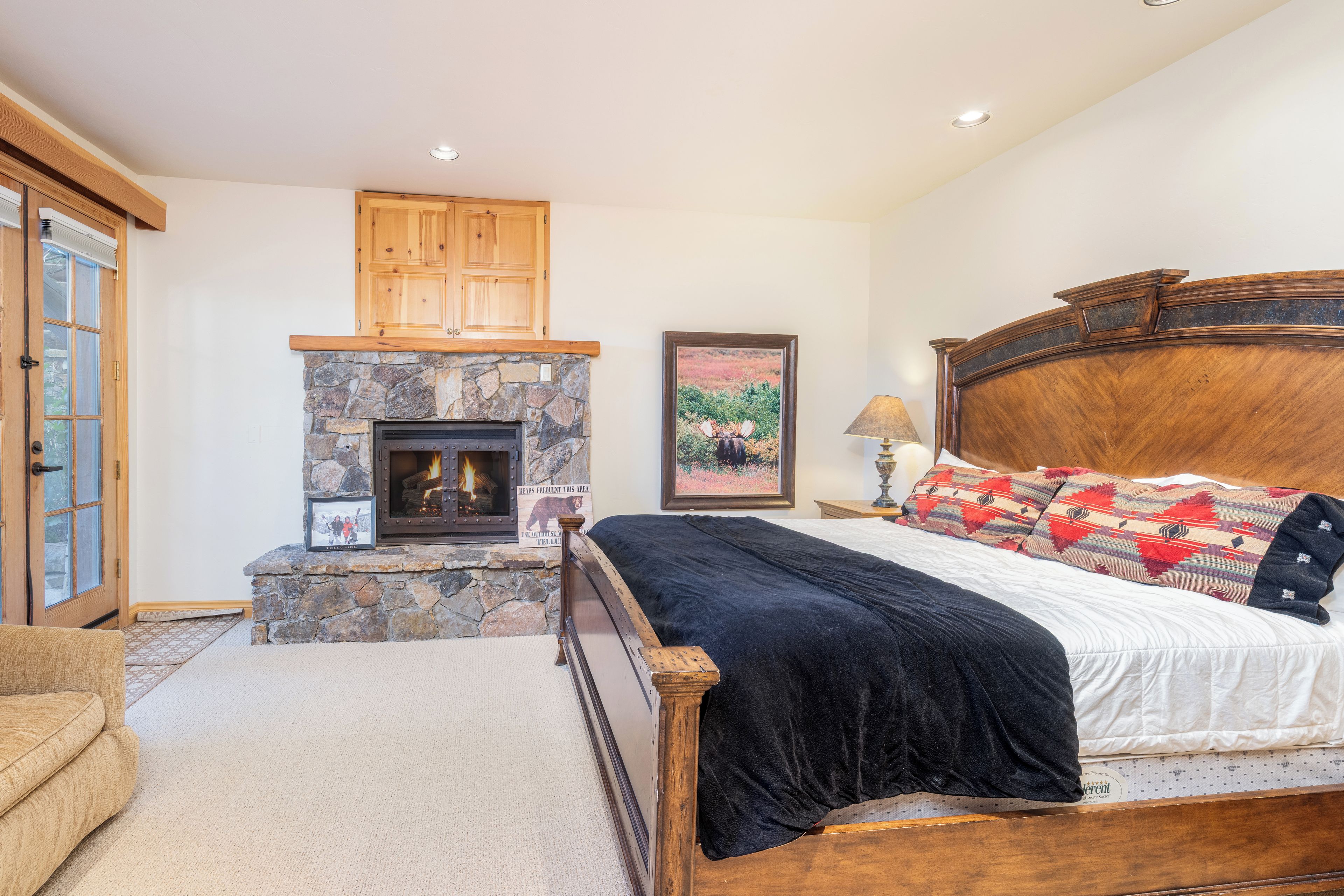 A bedroom with a stone fireplace, wooden headboard, and a bed with a black comforter.
