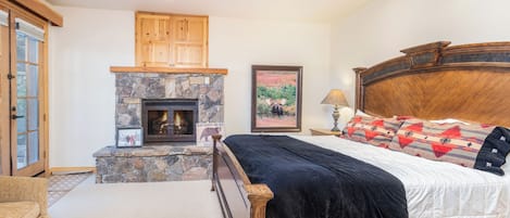 A bedroom with a stone fireplace, wooden headboard, and a bed with a black comforter.