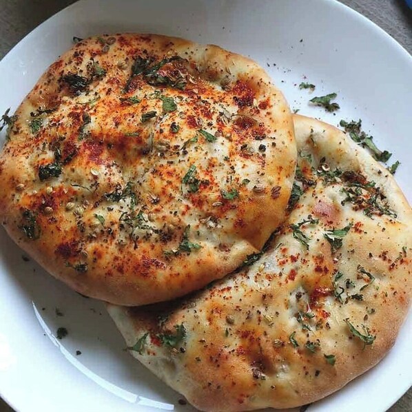 A white plate with two pieces of flatbread topped with herbs and spices. - Hotel Golden Heaven Inn Amritsar (Amritsar)