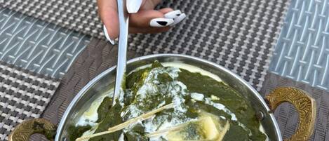 A bowl of spinach dish with a spoon, placed on a woven table mat.