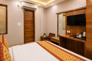 Quarto de hotel com uma cama, uma escrivaninha, uma cadeira, uma televisão e um guarda-roupa.