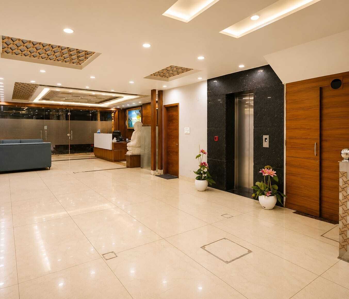 Un hall de hotel con un mostrador de recepción, una estatua, un ascensor y plantas en macetas.