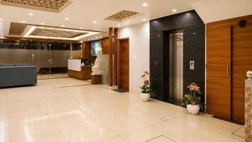 Un hall de hotel con un mostrador de recepción, una estatua, un ascensor y plantas en macetas.
