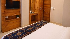 Una camera da letto con un letto, una televisione montata su un pannello di legno, un armadio e una piccola mensola con una pianta.