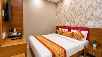 Une chambre d’hôtel avec un lit, une table de chevet, une petite plante et un téléviseur fixé au mur.