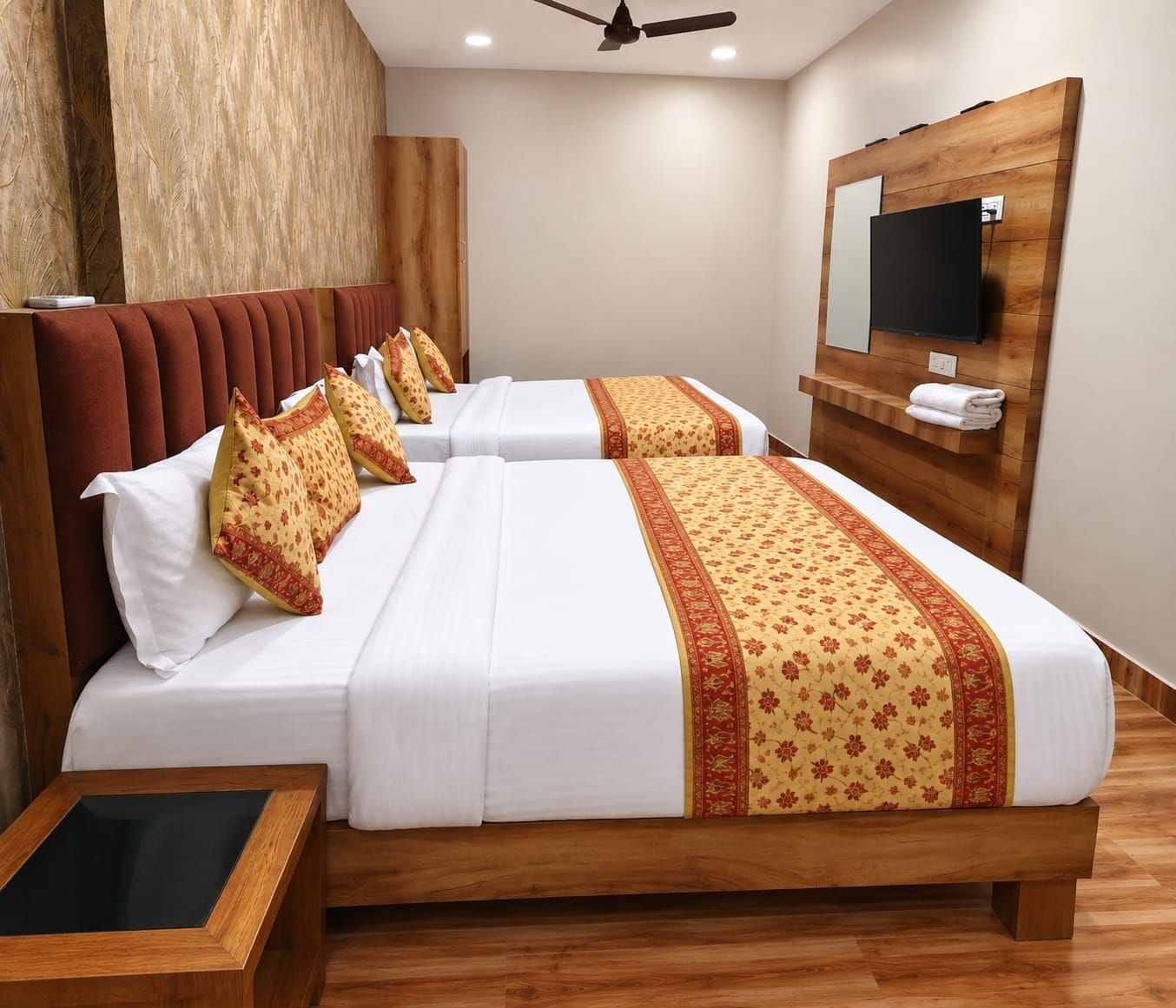 A hotel room with two beds, a wooden headboard, a flat-screen TV mounted on the wall, and a wooden floor.