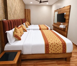 Une chambre d’hôtel avec deux lits, une tête de lit en bois, un téléviseur à écran plat fixé au mur et un plancher en bois.