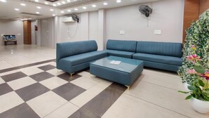 A modern lobby with a checkered floor, a blue sectional sofa, a glass coffee table, and a potted plant. - Hotel Golden Heaven Inn Amritsar (Amritsar)