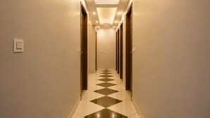 Un corridoio d'albergo con pavimento a scacchi, porte su entrambi i lati e illuminazione incassata.