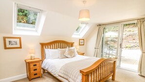 Un dormitorio con cama de madera, mesita de noche, lámpara y ventana con vistas al exterior.