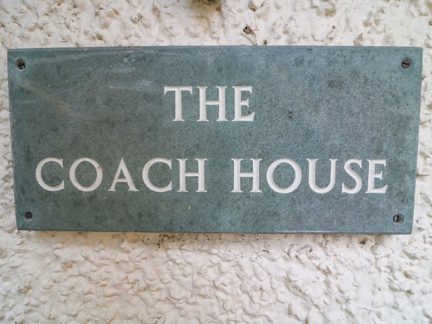 Une enseigne portant l’inscription « THE COACH HOUSE » est fixée à un mur à texture.
