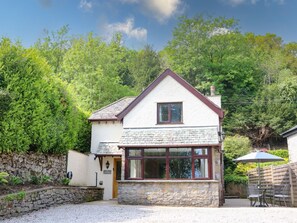 Une maison à deux étages, avec des fondations en pierre, un toit à deux versants et un petit porche à l’avant.