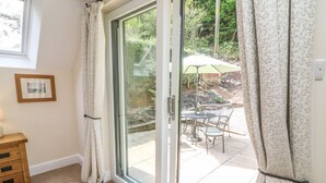 Una habitación con puerta de vidrio corredera que da a un patio exterior con mesa y sillas, un cuadro en la pared y un aparador de madera.
