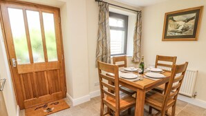 Un comedor con una mesa de madera dispuesta para cuatro, una puerta de madera y una ventana con cortinas.