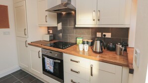 A modern kitchen with white cabinets, a stainless steel range hood, a built-in oven, and a wooden countertop. - Cliffe Cottage (Saltburn-by-the-Sea)