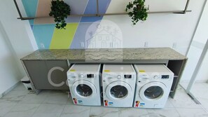 A laundry area with three Samsung washing machines, a tiled floor, and a wall with a colorful geometric design.