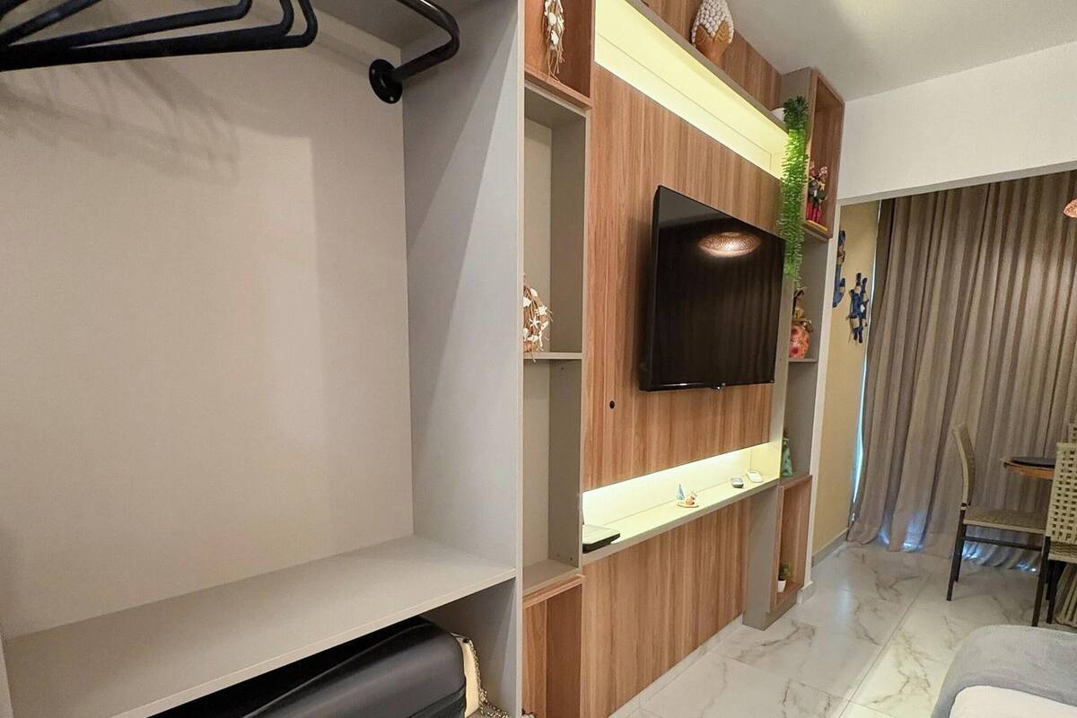 Une chambre d’hôtel comprenant un lit, un téléviseur fixé au mur, un porte-manteau et une petite étagère ornée d’objets décoratifs.