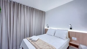 Une chambre d’hôtel avec un lit, des rideaux, des lampes de chevet, une table de chevet et un luminaire fixé au mur.