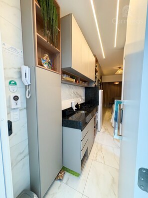 A modern kitchen with grey cabinets, a black countertop, and a built-in stove. There is a phone on the wall and a small plant on the shelf. - Waikiki Garden - Porto de Galinhas (Ipojuca)