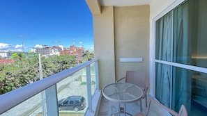 Ein Balkon mit Glasdoor, einem kleinen Tisch und Stühlen mit Blick auf eine Stadtlandschaft mit Gebäuden und einem Auto.