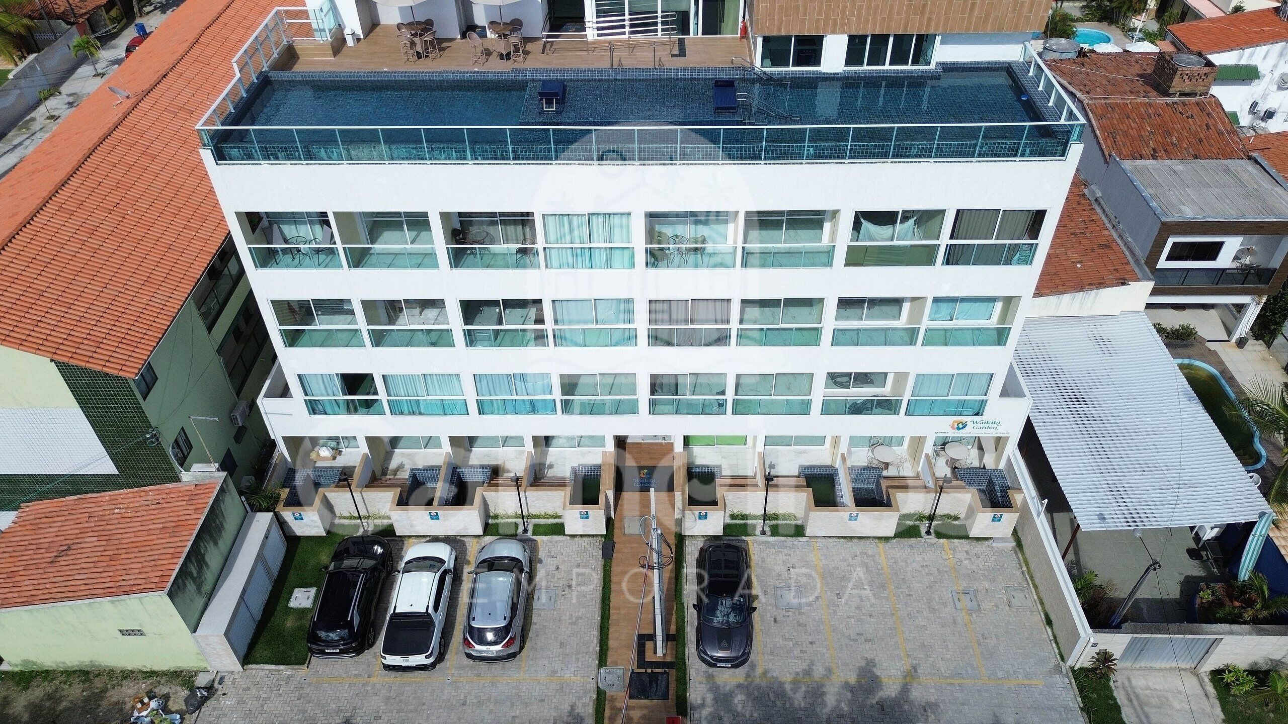 A multi-story building with a rooftop pool, a parking area with several cars, and a sign indicating a business center.