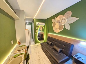 A modern living room with a sofa, a dining area with a table set, and a hallway leading to a bedroom. - Waikiki Garden - Porto de Galinhas (Ipojuca)