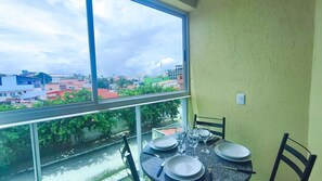 A dining area with a table set for two, a window with a view of buildings, and a chair.