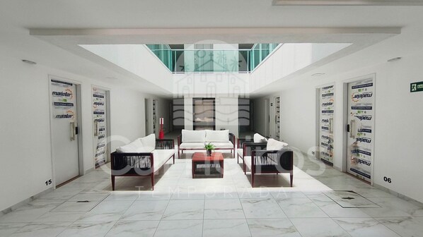 A spacious lobby with a high ceiling, a central seating area with a sofa and coffee table, and a glass railing overlooking the space.