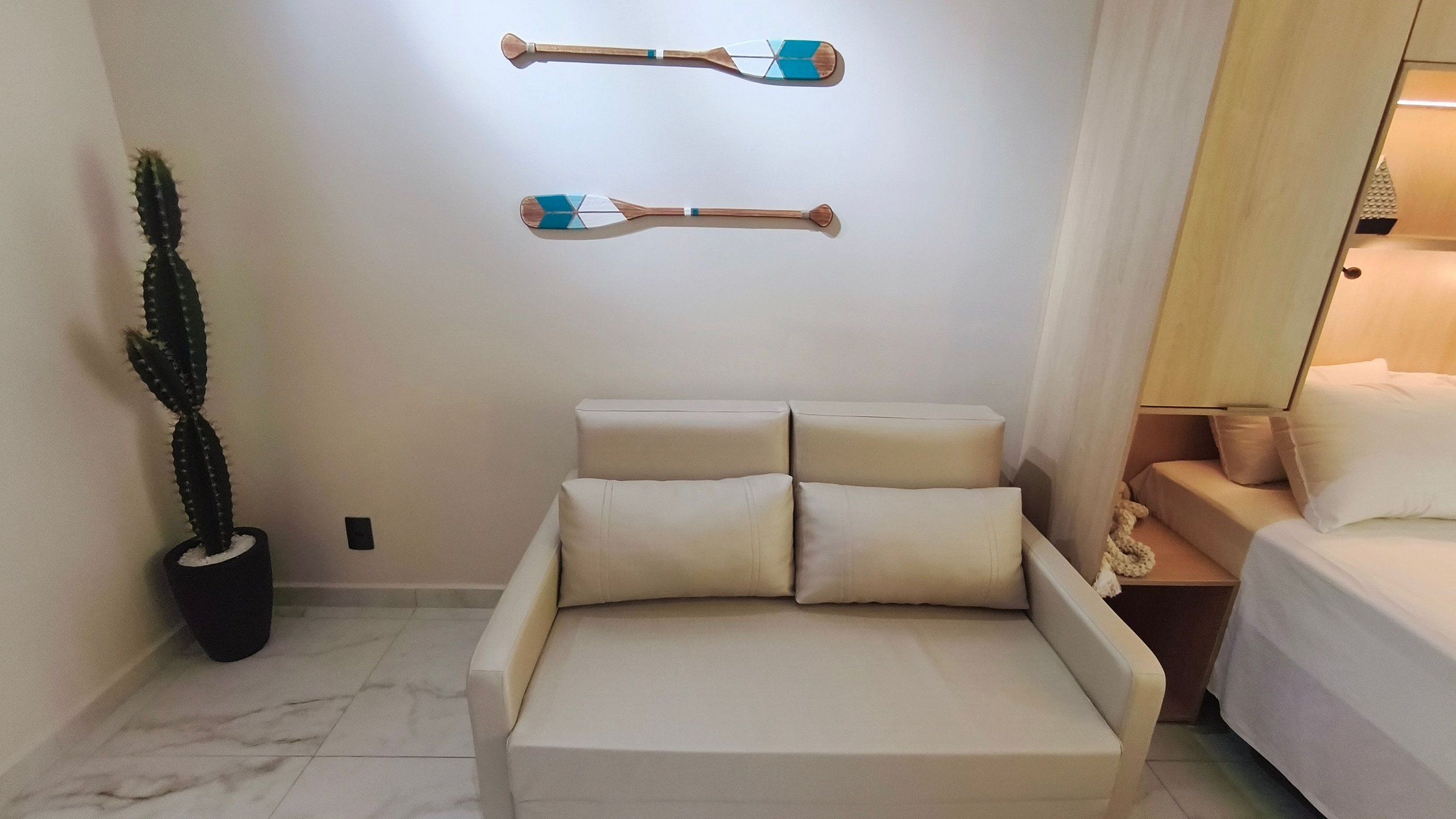 A minimalist room with a bed, a potted cactus, and two wall-mounted objects.