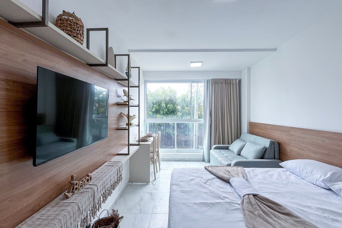 Une chambre d’hôtel moderne dotée d’un grand téléviseur à écran plat fixé au mur, d’un canapé, d’un lit et d’un coin repas avec une table et des chaises.