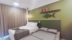 A hotel room with a bed, a sofa, a wall-mounted shelf with decorative items, and a fish mural. - Waikiki Garden - Porto de Galinhas (Ipojuca)