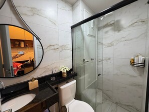 Une salle de bain moderne avec un sol en marbre, une douche en verre, des toilettes blanches, un plan de toilette noir et un miroir rond.