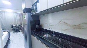Een kleine keuken met een koelkast, een koffiezetapparaat, een magnetron en een spoelbak.