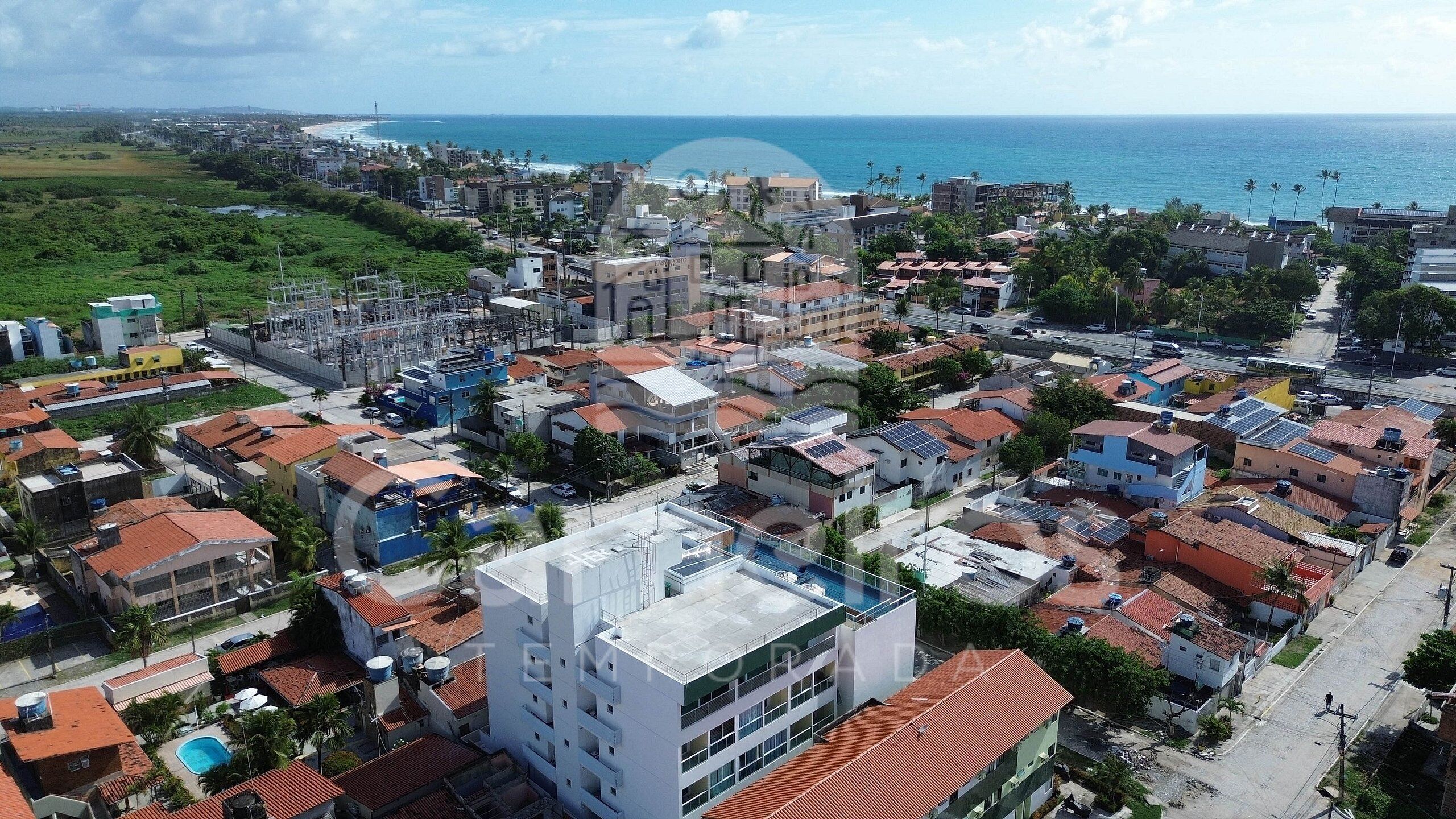 An urban area with residential buildings, a large industrial complex, and a view of the ocean.