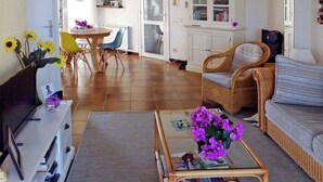 Ein Wohnzimmer mit einer Couch, einem Couchtisch mit Blumen, einem Fernseher und einem Essbereich mit Stühlen und Tisch.