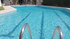 Ein klares Schwimmbecken mit Metallleiter, umgeben von einer angelegten Grünfläche mit Palmen und einer Hecke.