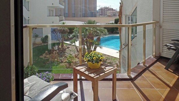 Ein Balkon mit Blick auf einen Swimmingpool, ein Tisch mit einer Topfpflanze und ein Stuhl.