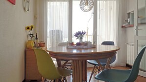 Ein Essbereich mit einem runden Tisch, vier Stühlen, einer Hängeleuchte und einem Fenster mit durchsichtigen Vorhängen.