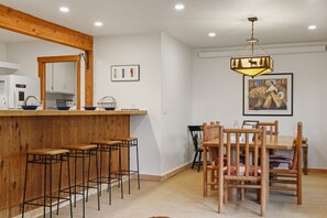 Un espace repas avec une table et des chaises en bois, un comptoir de bar avec des tabourets et un luminaire suspendu.