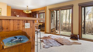 Una habitación amplia con un gran ventanal, techo de madera y decoración rústica que incluye una cabeza de ciervo y un cuadro.